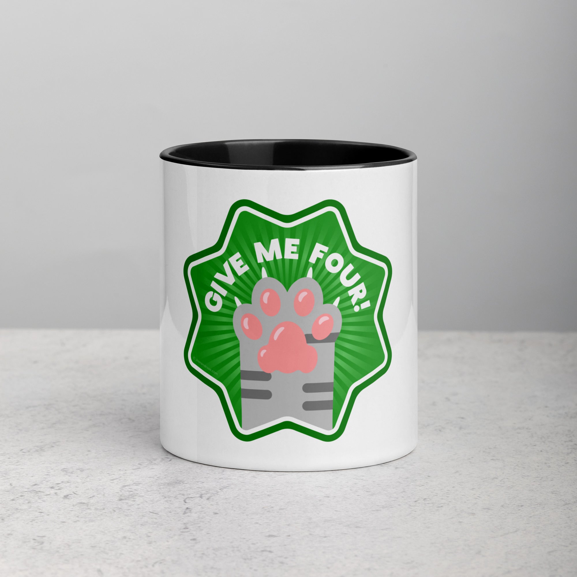front facing image of a white mug with black interior and handle. Mug has image of a grey tabby cats paw on a green 8 sided star with the text 'give me four' 